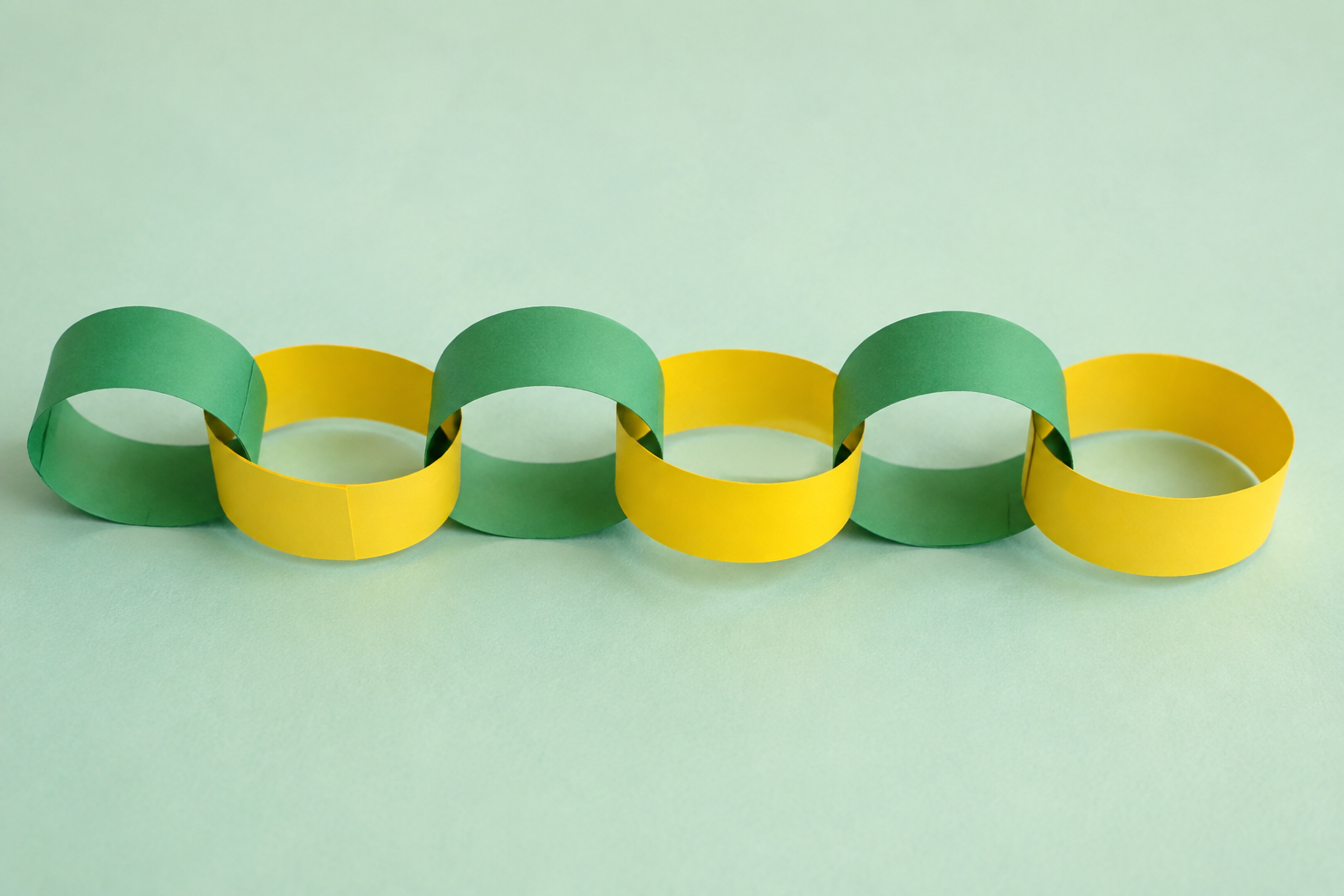 Een ketting van zes in elkaar gehaakte groene en gele papieren ringen, nog zonder kop.