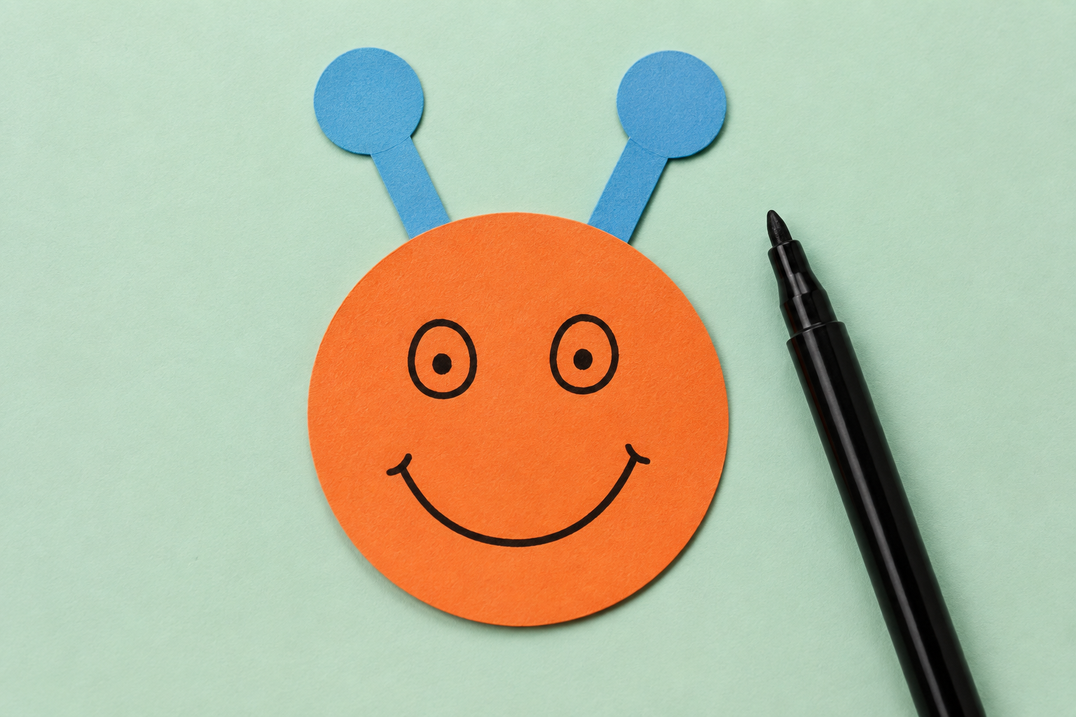 Een oranje papieren rondje met getekende ogen, een glimlach en twee papieren voelsprieten.