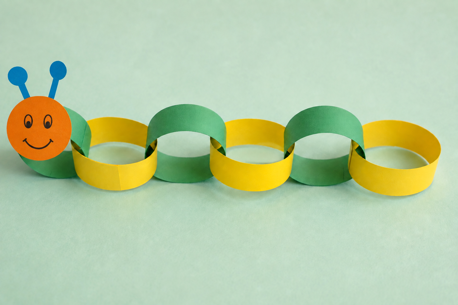 De afgewerkte papieren rups met een oranje gezicht en een lijf van groene en gele schakels.